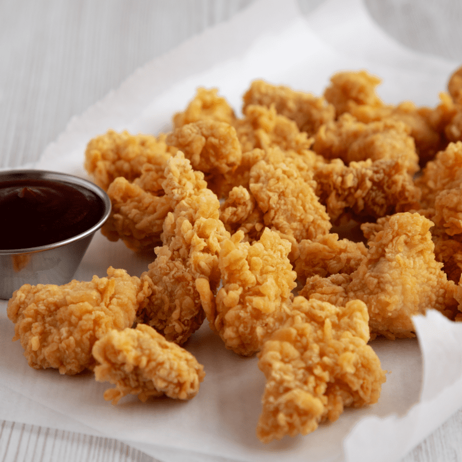Popcorn chicken on a white surface with a dipping sauce on the side