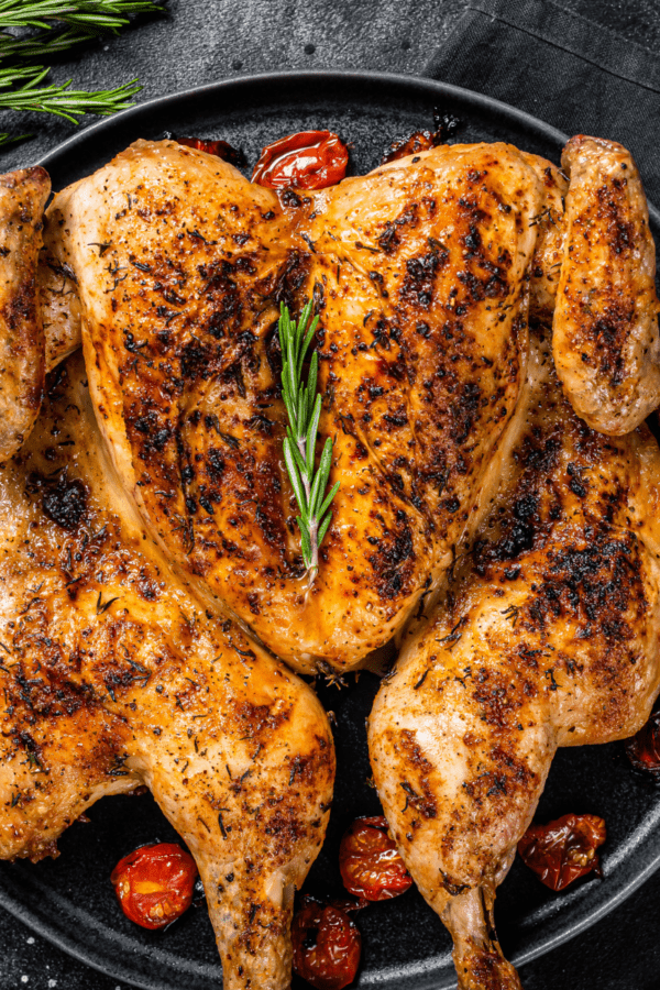 Spatchcock chicken in a pan with roasted tomatoes and herbs