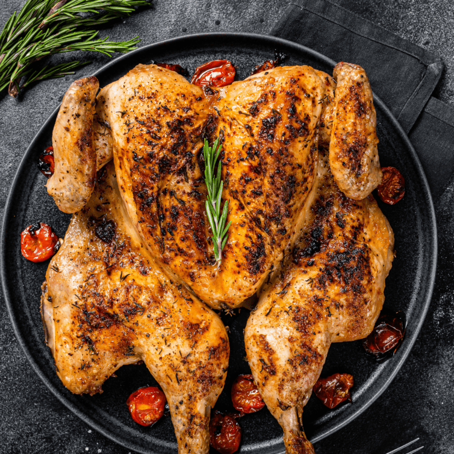 Spatchcock chicken in a pan with roasted tomatoes and herbs