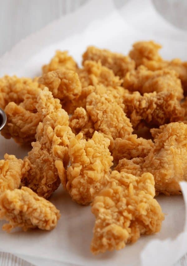 Popcorn chicken on a white surface with a dipping sauce on the side