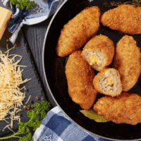 Chicken croquettes in a black skillet next to a gingham napkin and shredded parmesan cheese