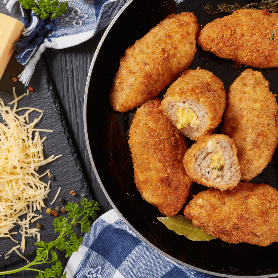 Chicken croquettes in a black skillet next to a gingham napkin and shredded parmesan cheese