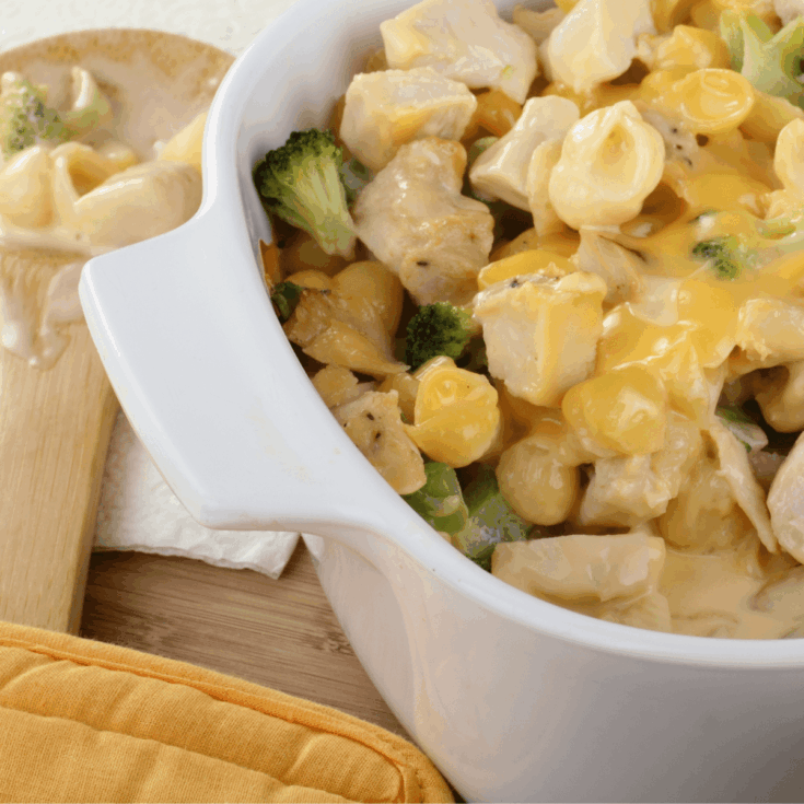 Closeup image of chicken divan in a white casserole dish with a wooden spoon in the background