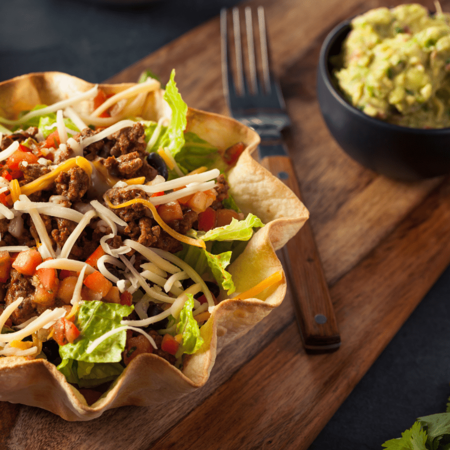 Taco Salad on a wooden serving platter with a fork and a side of guacamole