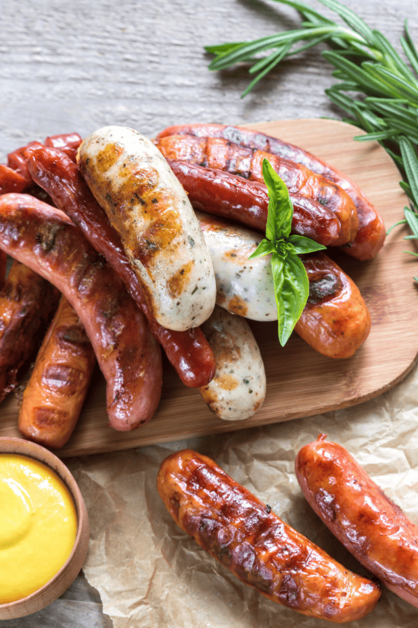 A variety of air fryer brats on a serving platter with mustard dipping sauce