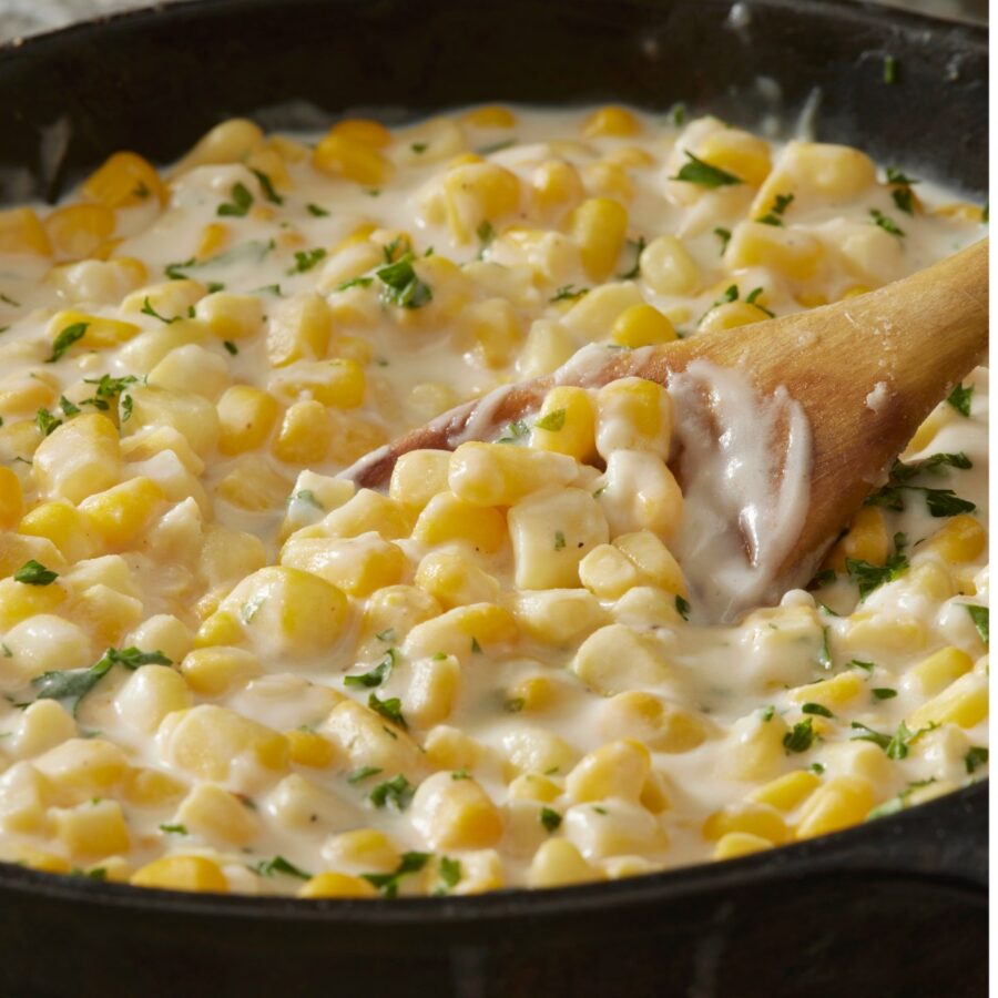 Creamed Corn in a skillet with a wooden spoon