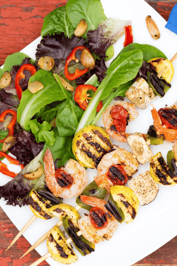 overhead view of shrimp kabobs on a white plate with a side salad