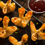 Air Fryer Crab Rangoon on a black platter with dipping sauce