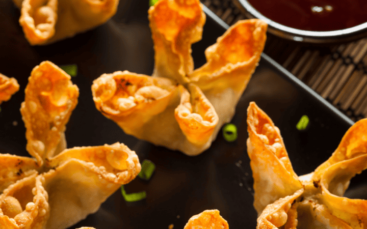 Air Fryer Crab Rangoon on a black platter with dipping sauce