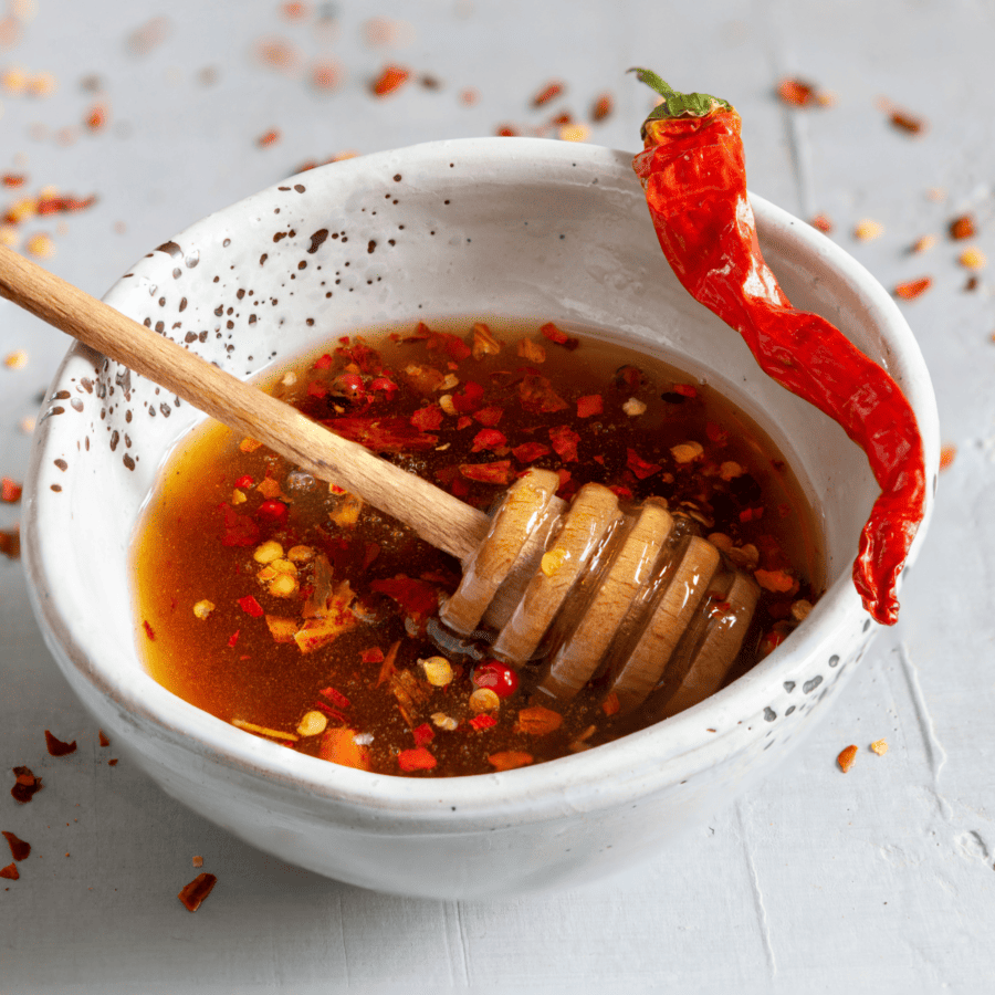 Hot Honey Sauce in a white bowl with a honey drizzler