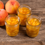 Three jars of peach pie filling in glass jars on a wooden table