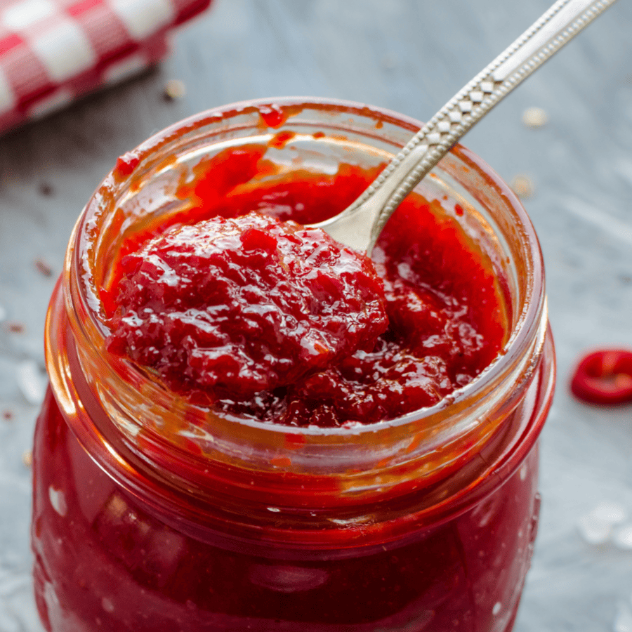 Close up of tomato jam in a glass jar with a spoon
