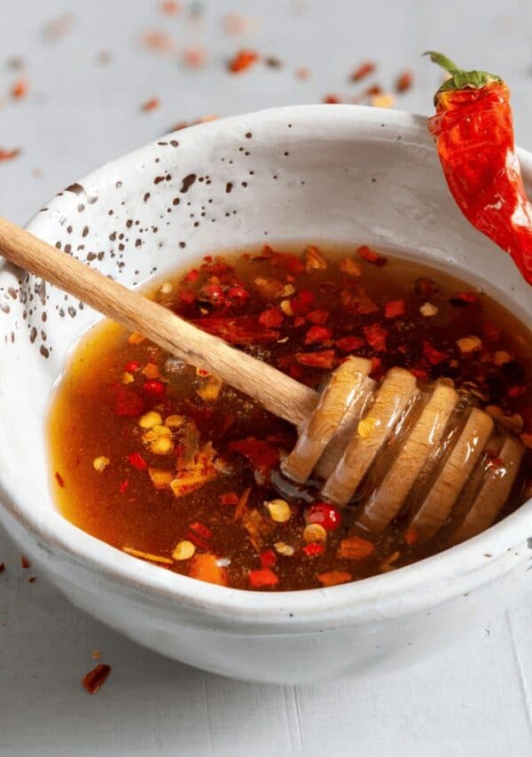 Hot Honey Sauce in a white bowl with a honey drizzler