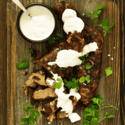 Sliced meat on a cutting board with Alabama White Sauce drizzled over the top