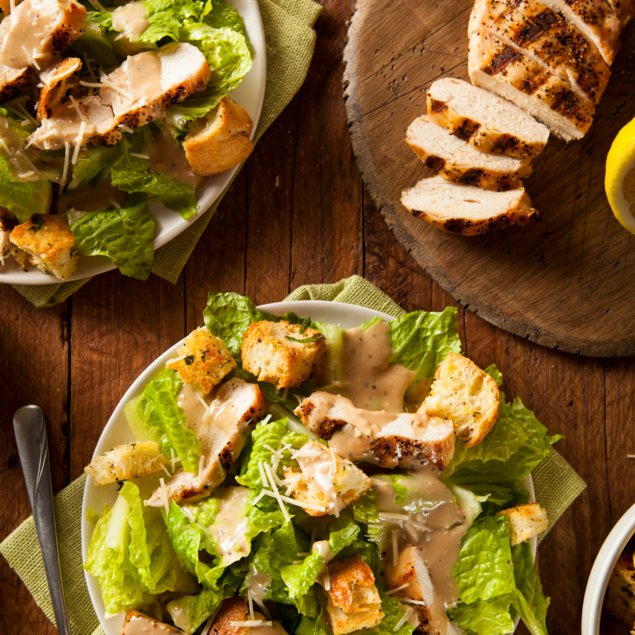 Two Chicken Caesar Salads on plates on a wooden table