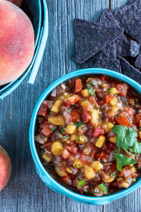 Overhead image of Peach Salsa in a blue bowl with peaches next to it