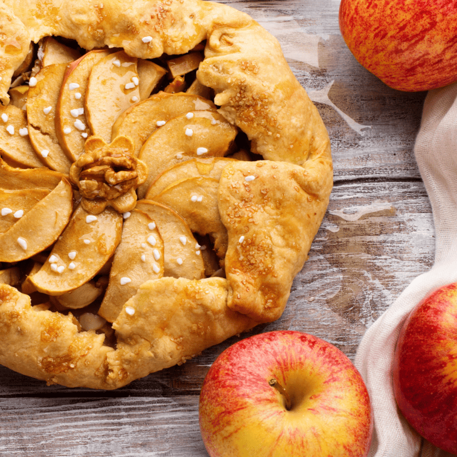 Close up image of an apple galette surrounded by red and yellow apples
