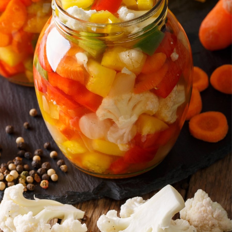 close up image of Giardiniera in glass jars surrounded by chopped vegetables