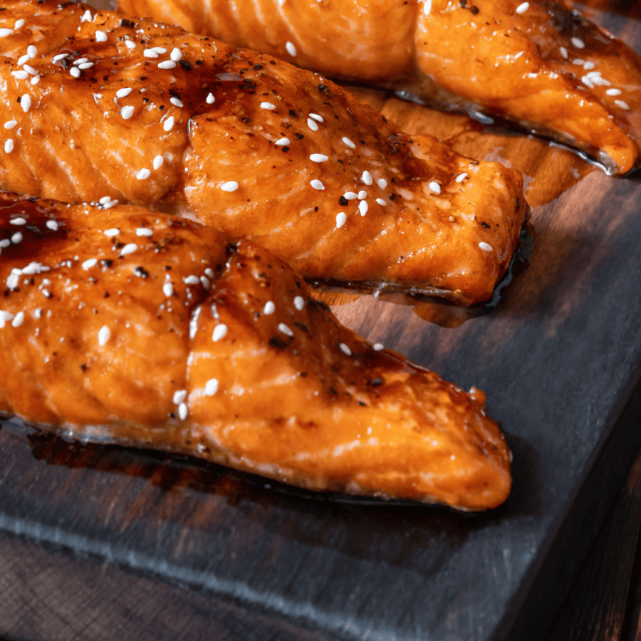 Close up of honey glazed salmon on a cutting board sprinkled with sesame seeds