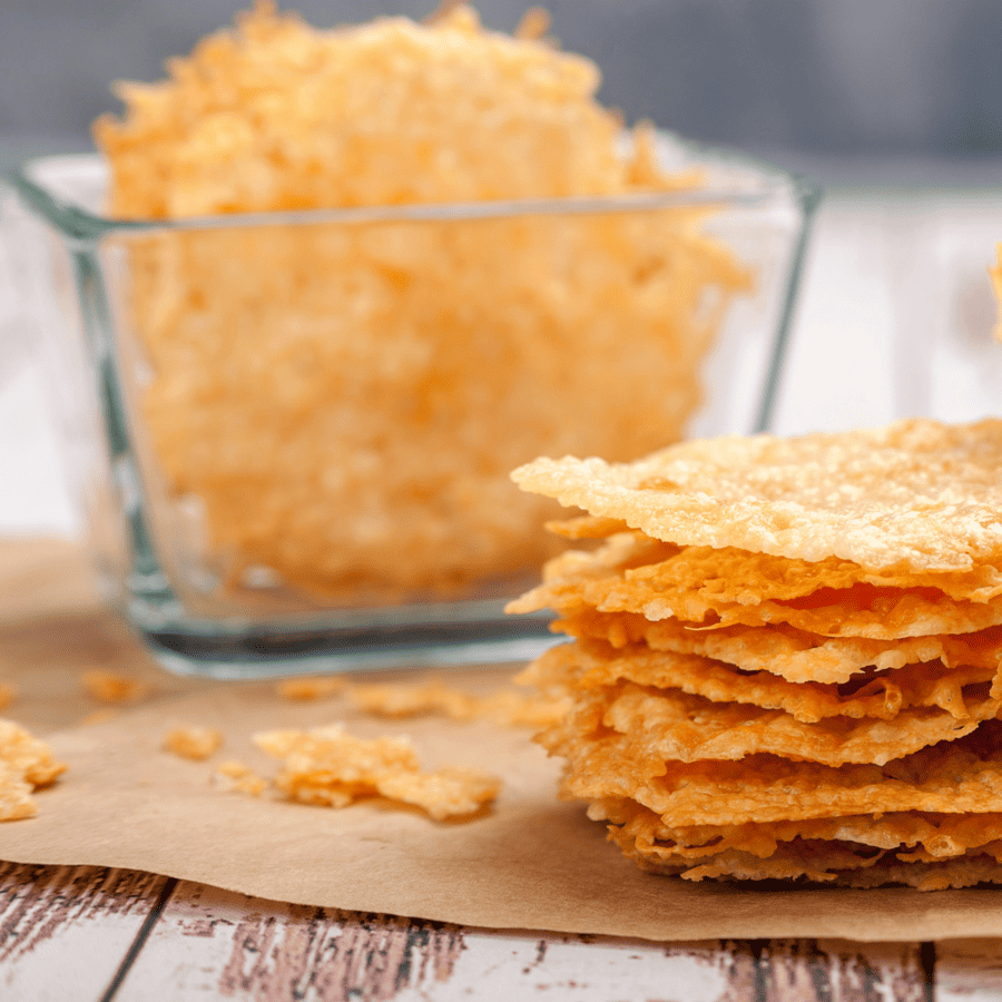 Parmesan crisps in a square glass bowl with more stacked to the side