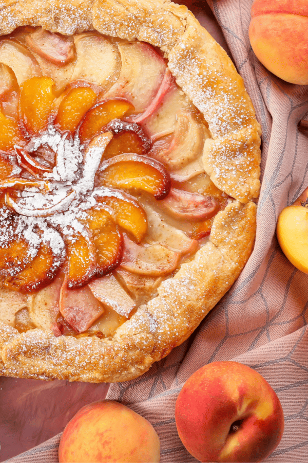 Close up of a peach galette surrounded by fresh peaches