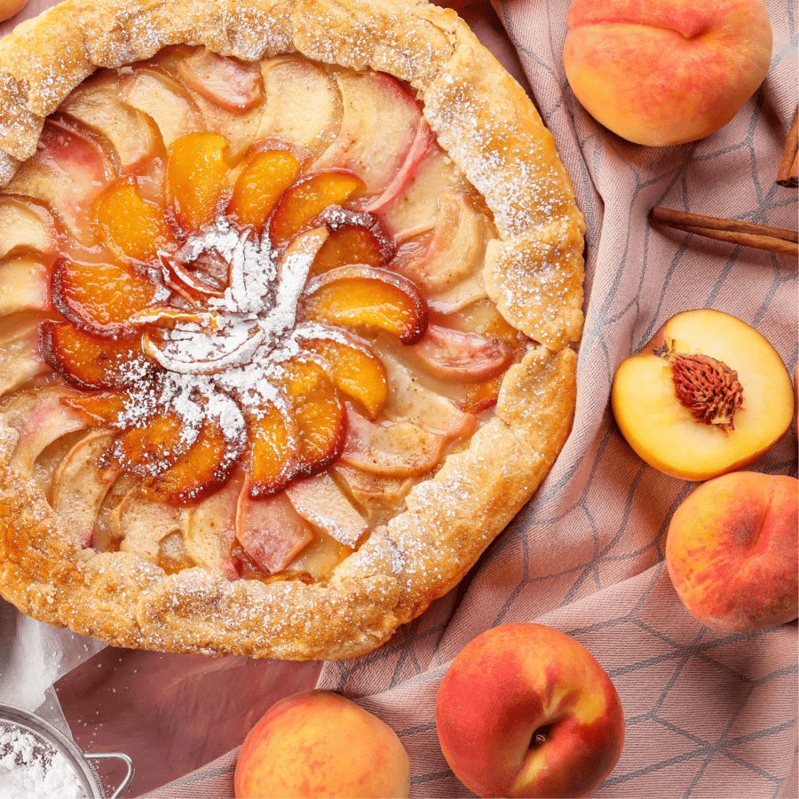 Close up of a peach galette surrounded by fresh peaches