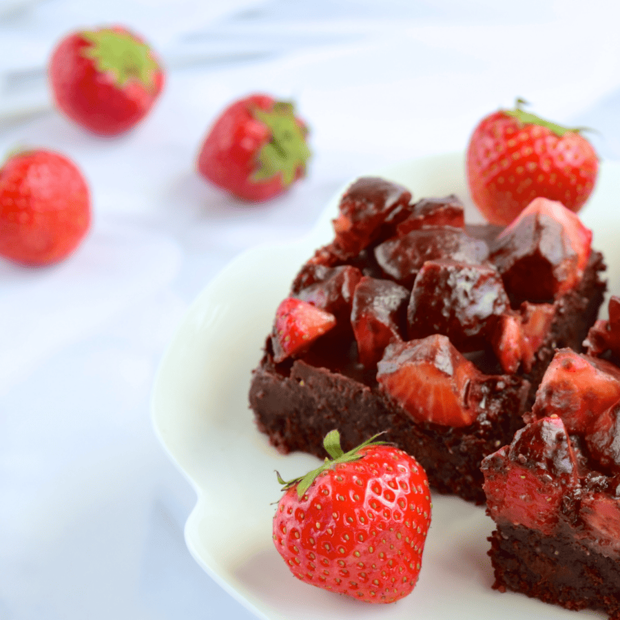 Close up image of strawberry brownies on a white plate surrounded by strawberries