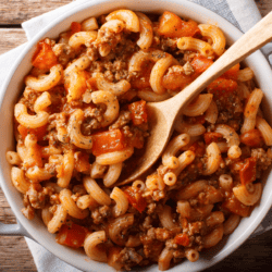 Overhead image of American Goulash in a white bowl with a wooden spoon