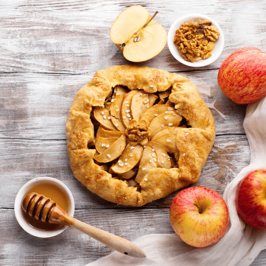 Apple Galette surrounded by apples and honey on a wooden backdrop