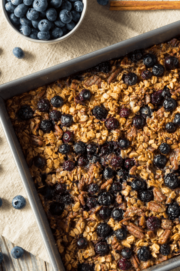 Blueberry Baked Oatmeal in a square pan surrounded by blueberries on a table