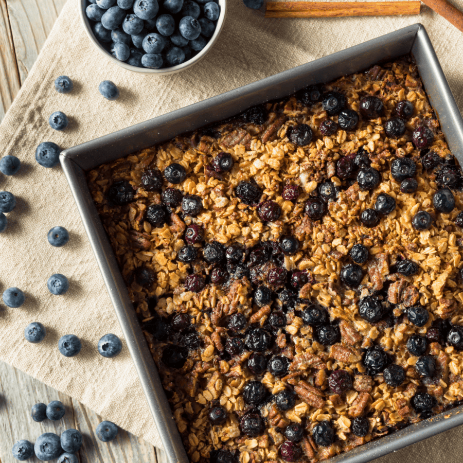 Blueberry Baked Oatmeal in a square pan surrounded by blueberries on a table