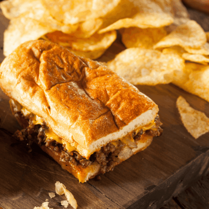 Close Up of a Chopped Cheese Sandwich on a wooden cutting board with a side of kettle chips
