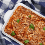 Closeup image of Crockpot BBQ Chicken in a dish on top of a plaid tablecloth