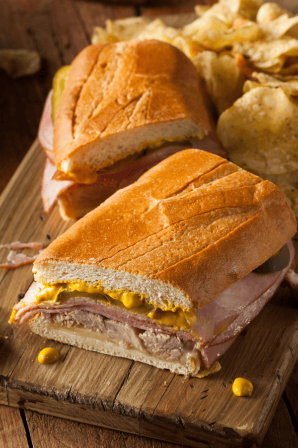 Two halves of a Cuban Sandwich on a wooden cutting board with chips