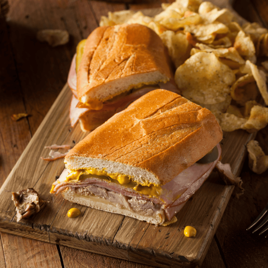Two halves of a Cuban Sandwich on a wooden cutting board with chips