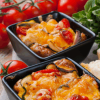 Two square bowls of taco casserole with tomatoes and lettuce in the background