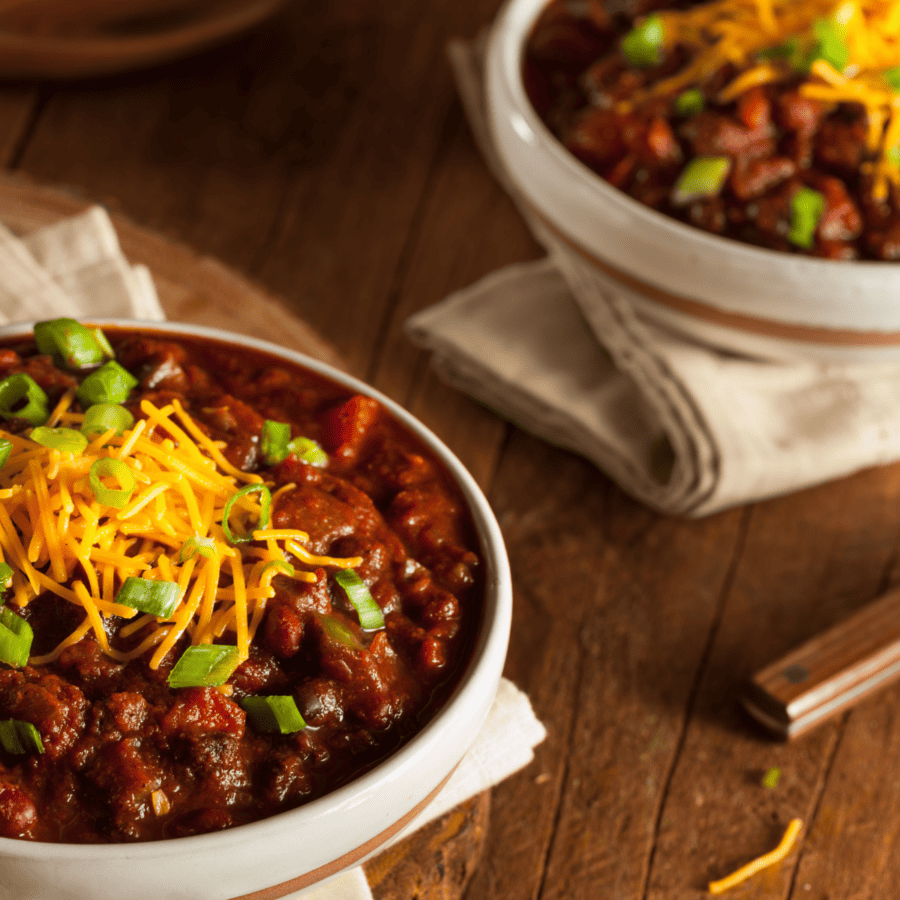 Closeup image of two bowls of crockpot chili on a wooden table