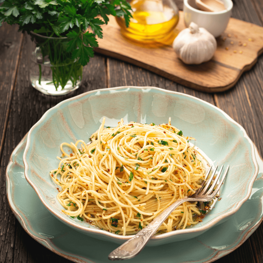 Garlic Noodles in a bowl on a saucer with garlic and herbs in the background