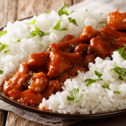 Bourbon chicken on a black plate with white rice surrounding it
