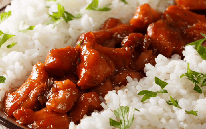 Bourbon chicken on a black plate with white rice surrounding it
