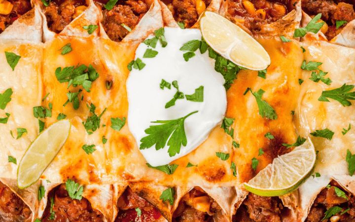 Vegetarian Enchiladas in a rectangular baking dish garnished with sour cream and lime