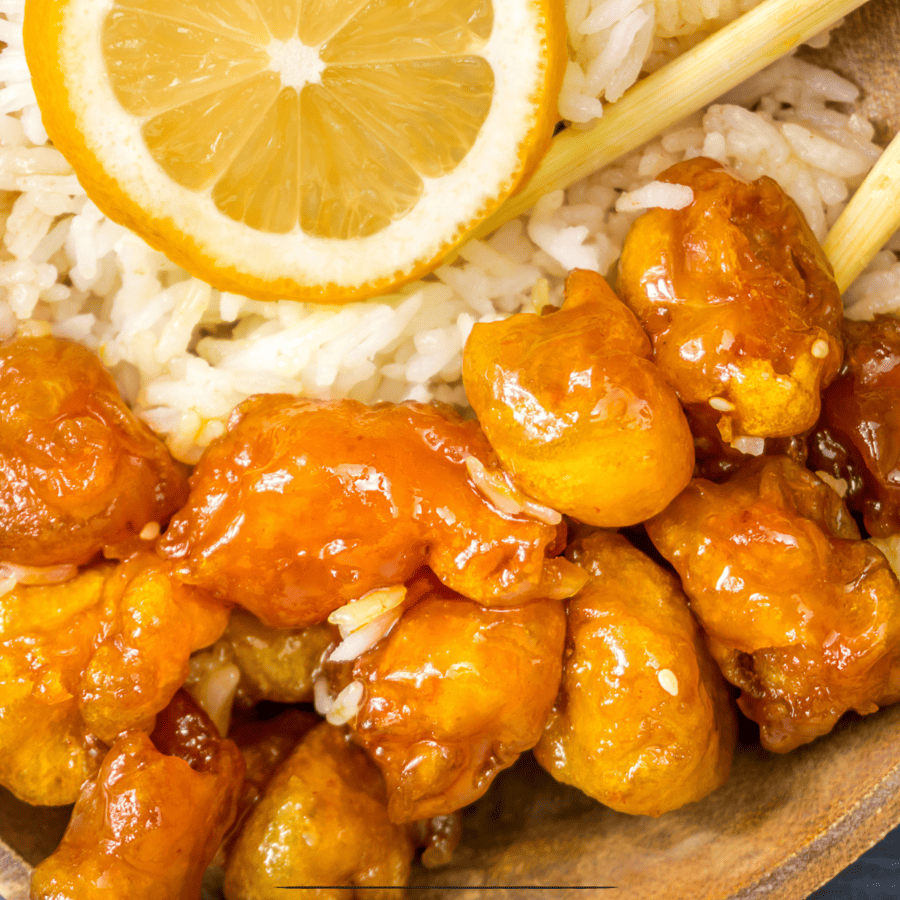 Close up image of Air Fryer Orange Chicken on a bed of rice with chopsticks and orange slice garnish