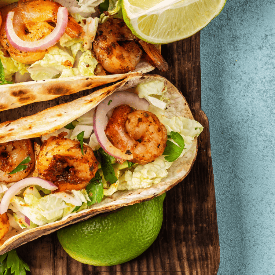 Close up image of Shrimp Tacos on a cutting board with limes for garnish