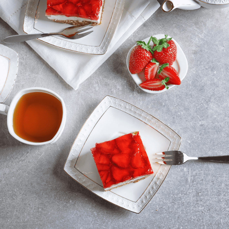 Overhead image of two pieces of Strawberry Pretzel Pie on square plates with sides of strawberries and tea