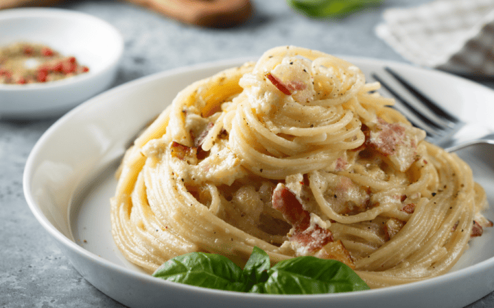 A swirled portion of Bacon Pasta on a white high-rimmed plate