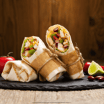 Three Grilled Chicken Wraps in a paper wrapper against a rustic background