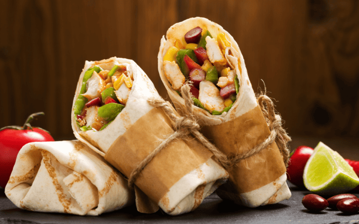 Three Grilled Chicken Wraps in a paper wrapper against a rustic background