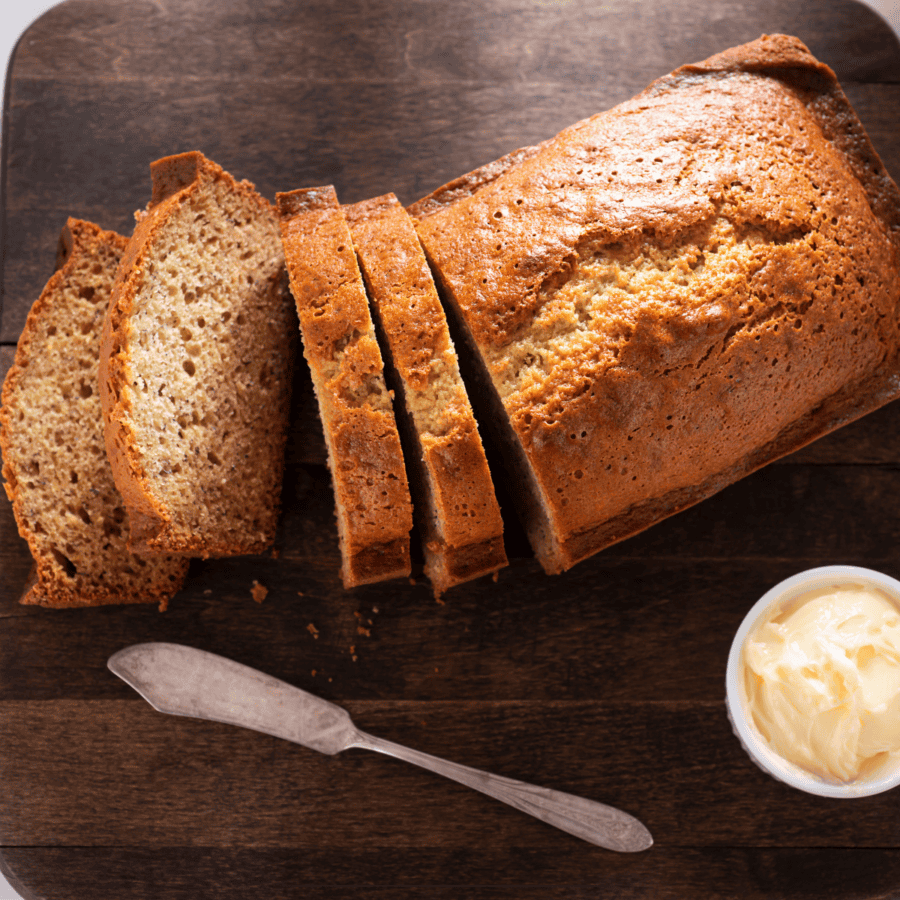 gluten free banana bread loaf with 4 slices cut and a small bowl of butter