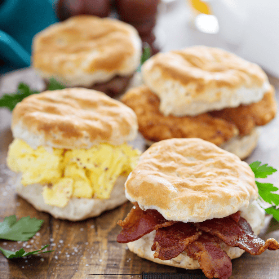 Overhead image of four biscuit sandwiches with scrambled eggs and bacon