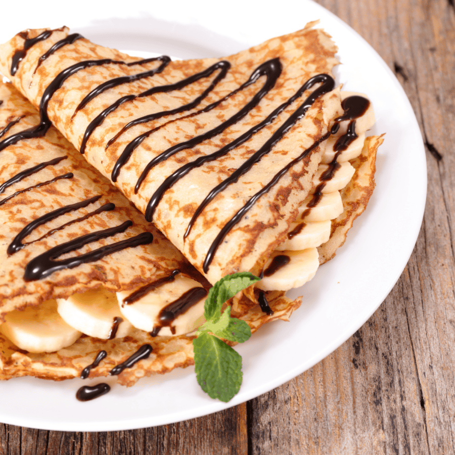 Close up image of breakfast crepes filled with bananas and drizzled with chocolate